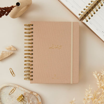 2025 planner with a soft cream-coloured fabric cover, featuring elegant gold details and ring binding, offering day-to-view pages, weekly overviews, and monthly spreads.