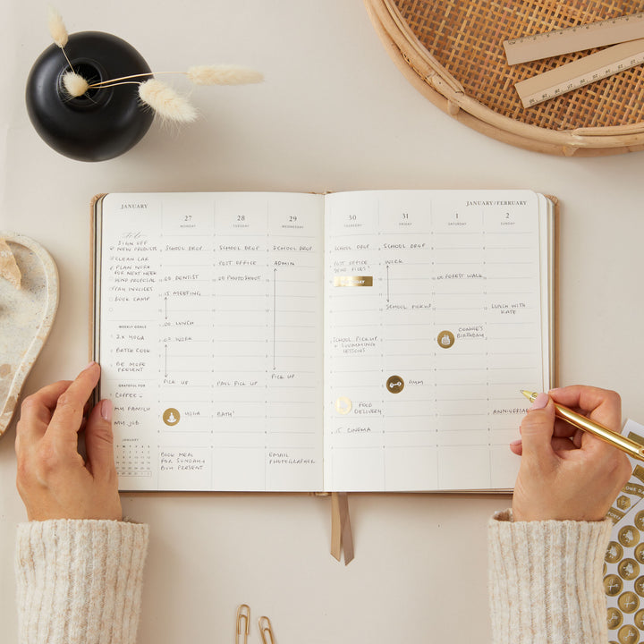 Ivory fabric 2025 weekly planner with gold accents, designed with time-blocking for each day, along with to-do lists, note space, and monthly goals and budgeting sections.