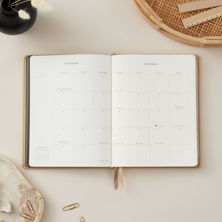 Elegant 2025 weekly planner with an ivory fabric cover and gold details, including equal daily time-blocking, to-do lists, notes, and monthly goal and budget pages.