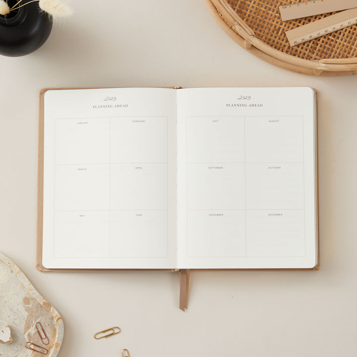 2025 weekly planner with an ivory fabric cover and gold details, featuring equal space for daily time-blocking, to-do lists, and dedicated sections for monthly goals and budgets.