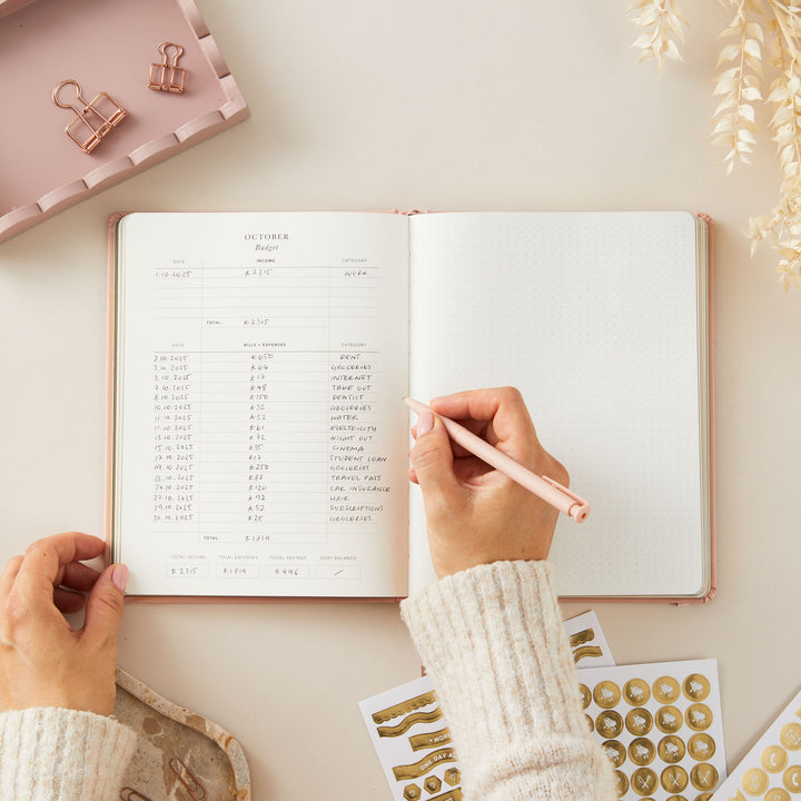 2025 weekly planner with a soft pink vegan leather cover and gold accents, featuring equal space for time-blocking each day, to-do lists, notes, and monthly goals and budget pages.