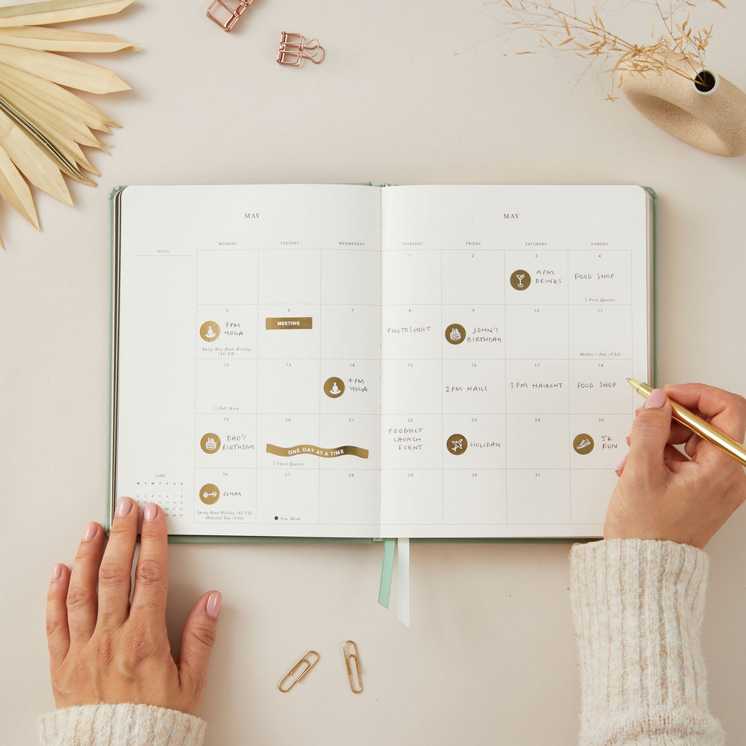 Stylish 2025 weekly planner with a sage green vegan leather cover and gold details, featuring time-blocking for each day of the week, to-do lists, and monthly goals and budgeting pages.