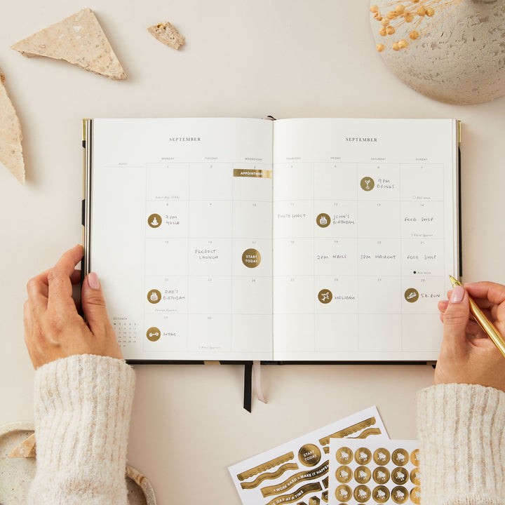 Elegant 2025 weekly planner with a minimalist floral design, gold foil cover, and gold edging, including time blocking, to-do lists, and sections for notes.