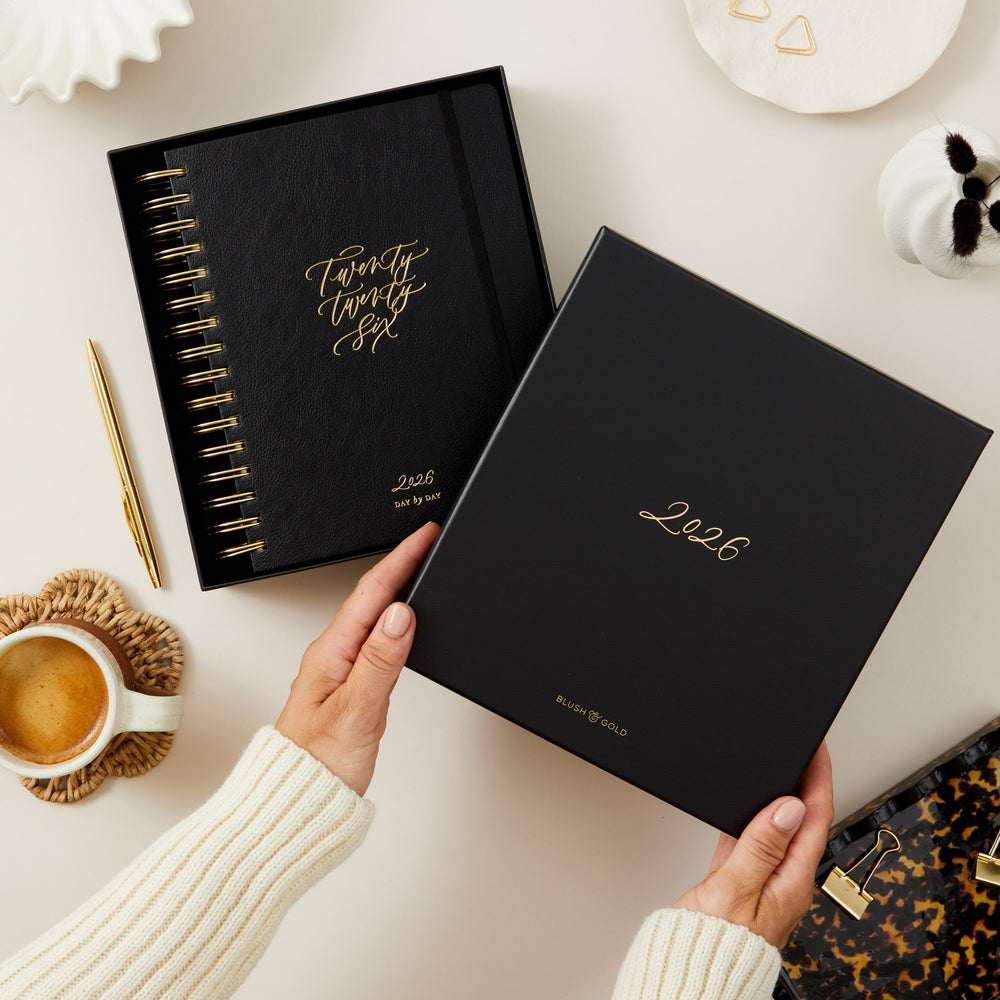 Black diary with '2026' embossed on them, held by a person on a light surface.