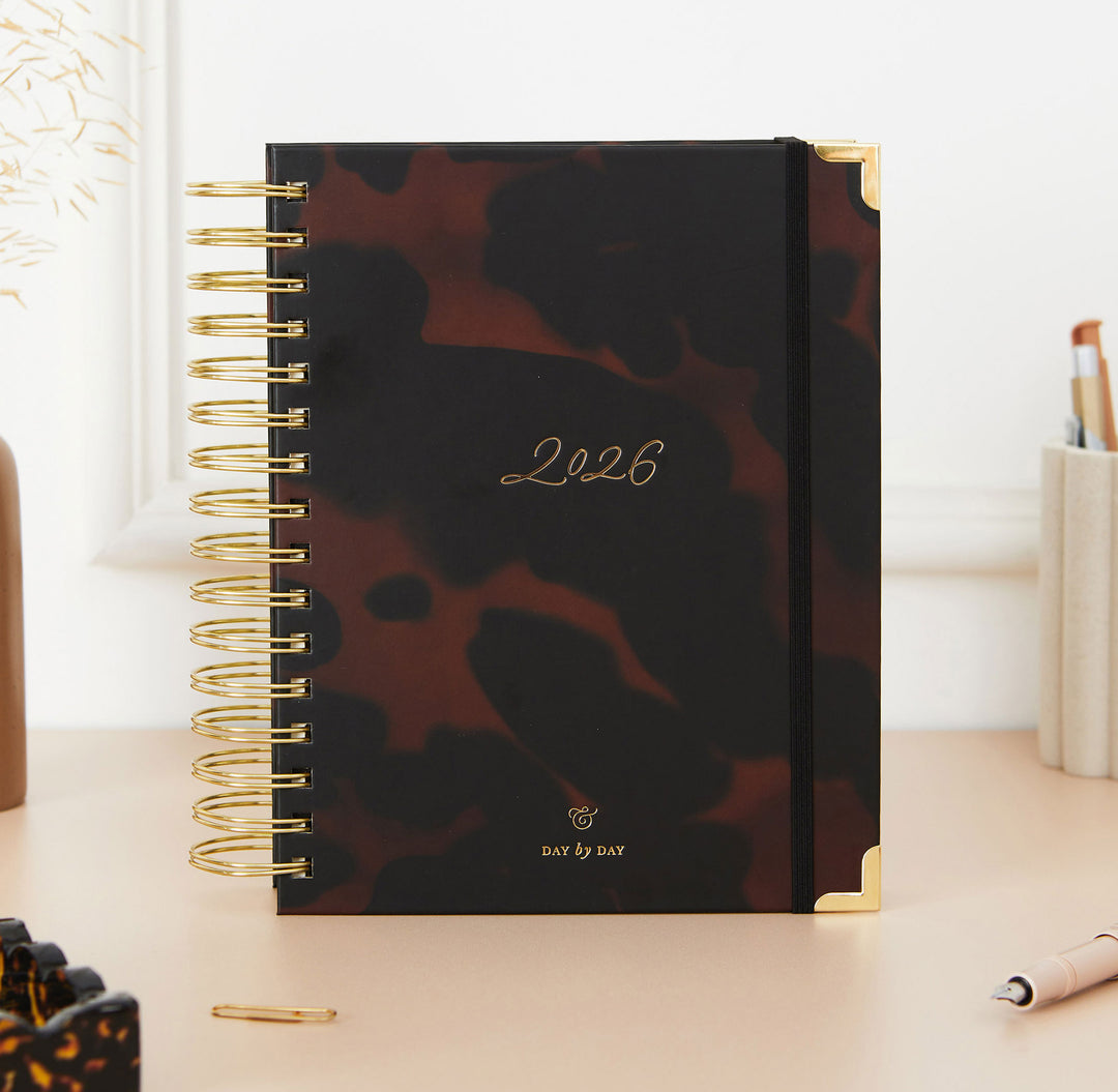 Dark patterned daily planner with '2026' on a desk with office supplies