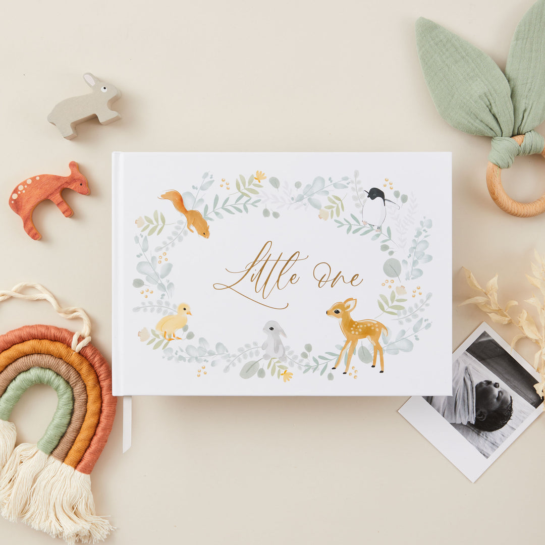 Cover of a baby memory book with an elegant illustration of cute animals and gold gilt edging, featuring delicate gold accents and a central title that reads 'Little One' in stylish gold lettering