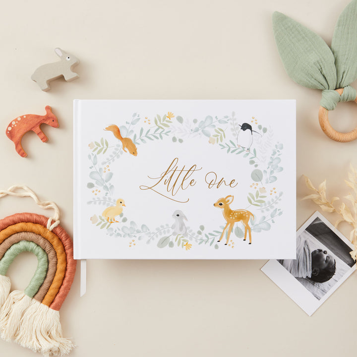 Cover of a baby memory book with an elegant illustration of cute animals and gold gilt edging, featuring delicate gold accents and a central title that reads 'Little One' in stylish gold lettering