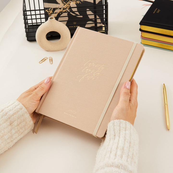 2025 planner with an ivory fabric cover and gold details, offering weekly time blocking with equal space for each day, to-do lists, and monthly goals and budget tracking.