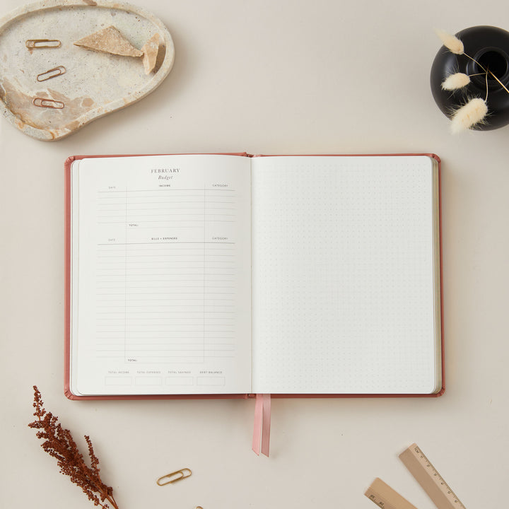 Luxurious 2025 planner with a clay vegan leather cover and gold details, offering equal space for time-blocking each day, to-do lists, and sections for monthly goals and budgets.