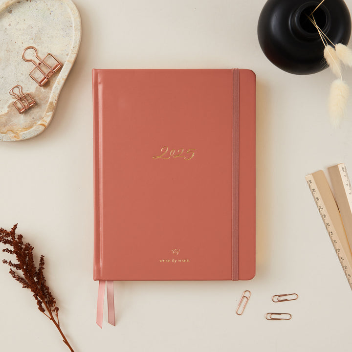 2025 planner with a clay vegan leather cover and gold details, offering weekly time-blocking, to-do lists, space for notes, and pages for tracking monthly goals and budgets.