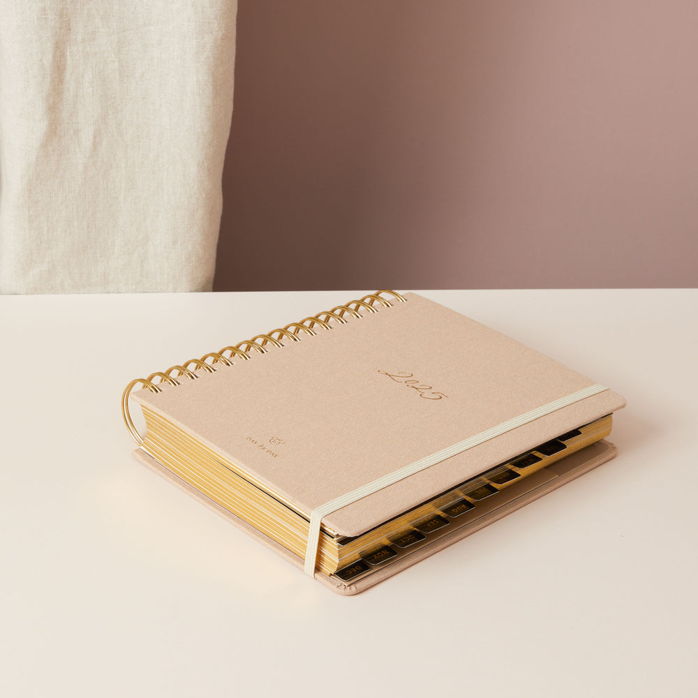 Cream-coloured 2025 planner with a soft fabric cover, gold accents, and a ring-bound design, including day-to-view, weekly, and monthly planning pages.