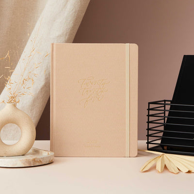 2025 weekly planner with an ivory fabric cover and gold details, featuring time-blocking for each day, to-do lists, space for notes, and monthly goals and budget pages.