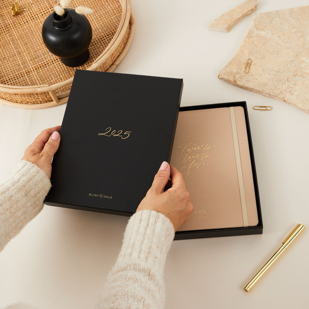 Ivory-covered fabric 2025 weekly planner with gold details, offering equal space for daily time blocking, to-do lists, notes, and sections for monthly goals and budgeting.
