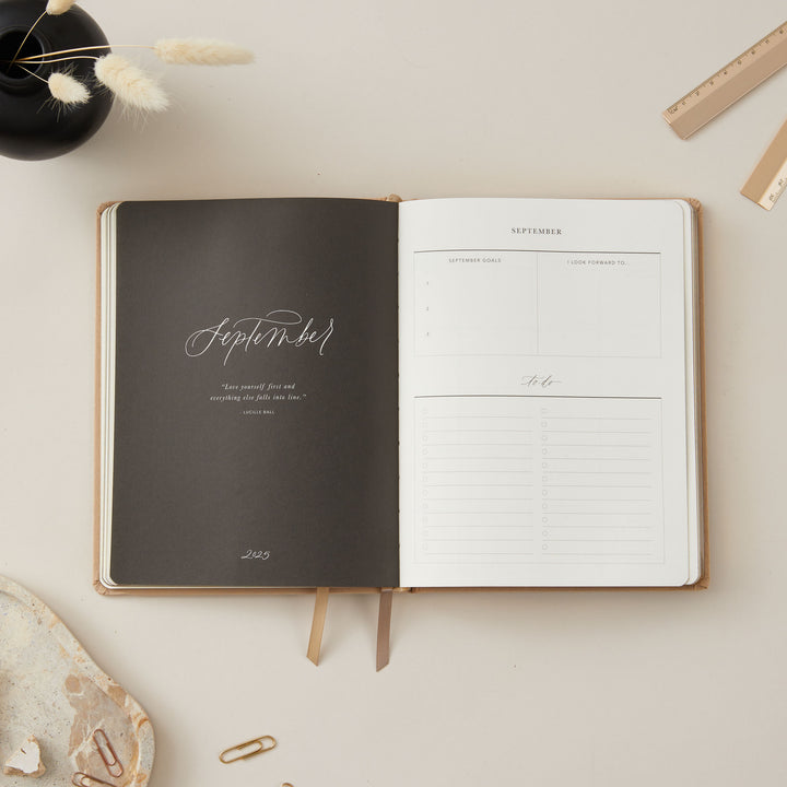 Ivory-covered fabric 2025 planner with gold details, providing equal time-blocking for each day, to-do lists, notes, and pages for tracking monthly goals and budgets.
