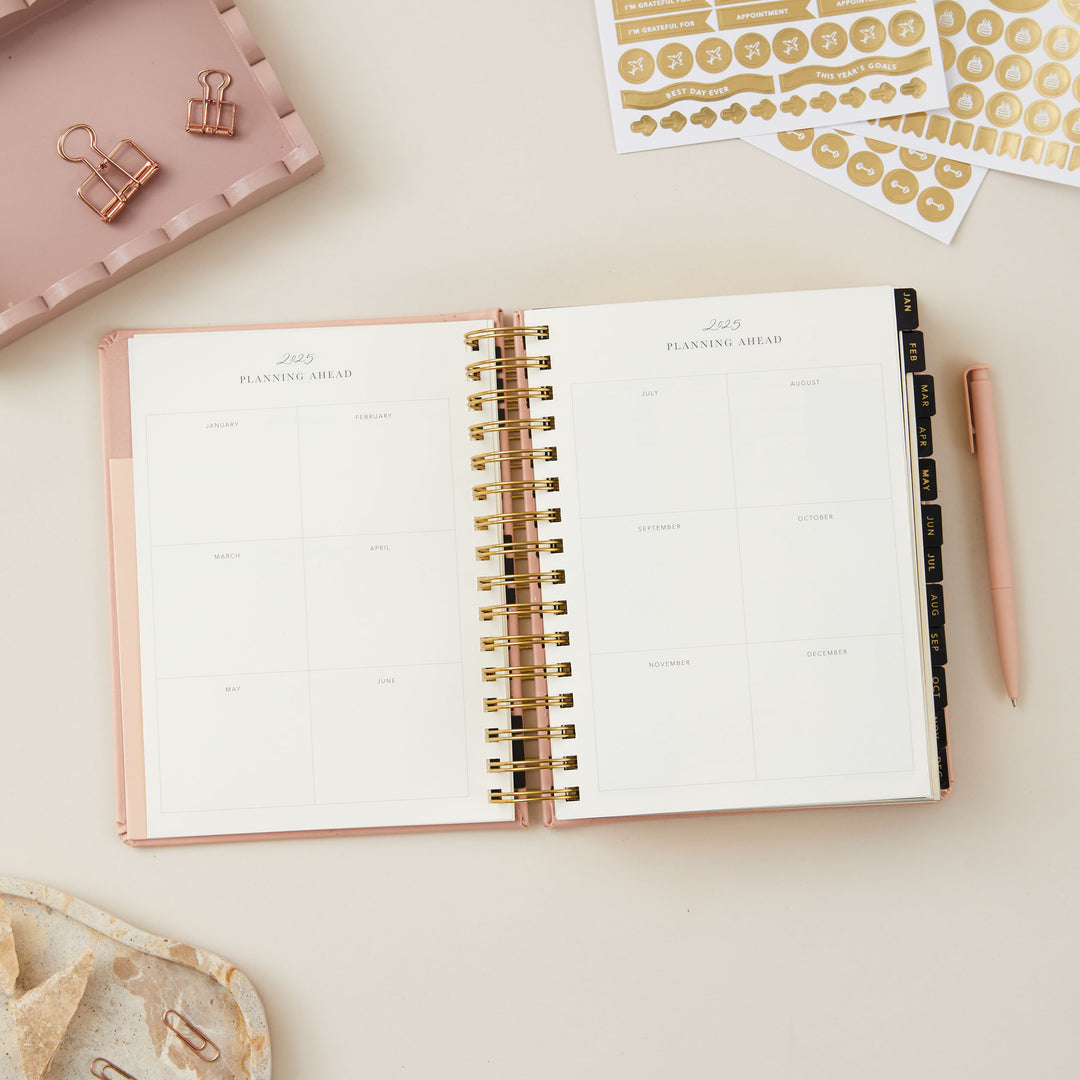 Elegant pink 2025 planner featuring day-to-view pages with areas for priorities, time-blocked daily schedule, to-do lists, notes, and meal planning.