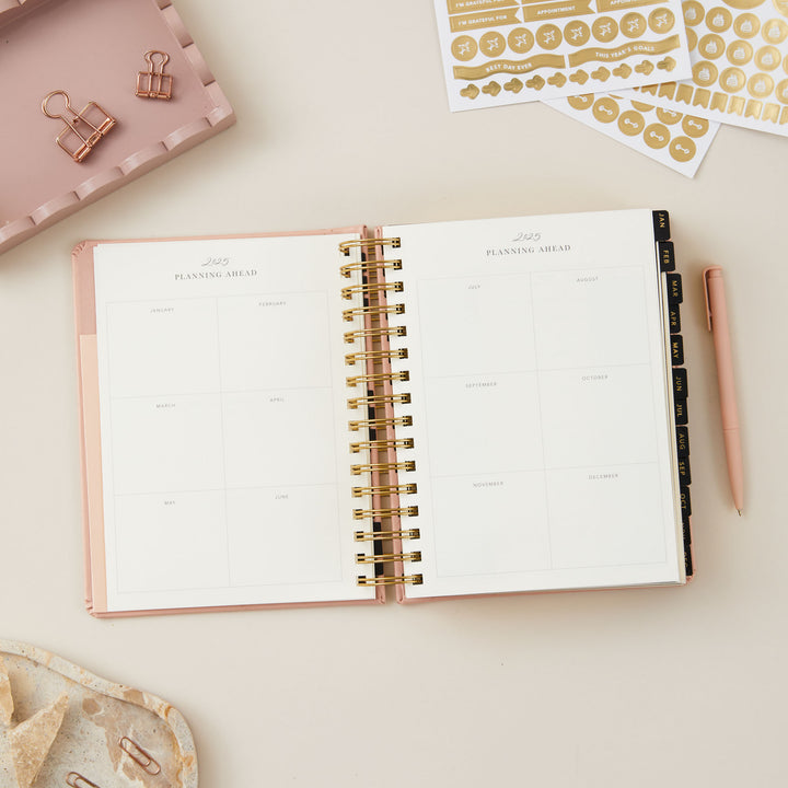 Elegant pink 2025 planner featuring day-to-view pages with areas for priorities, time-blocked daily schedule, to-do lists, notes, and meal planning.