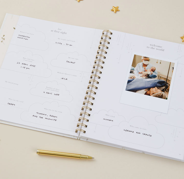 Open baby memory book with handwritten notes and a photo of a family on a beige surface.