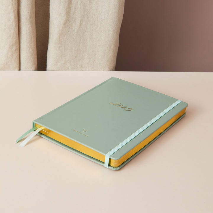 2025 planner with a sage green vegan leather cover and gold details, offering weekly time-blocking with equal space for each day, to-do lists, and sections for notes.