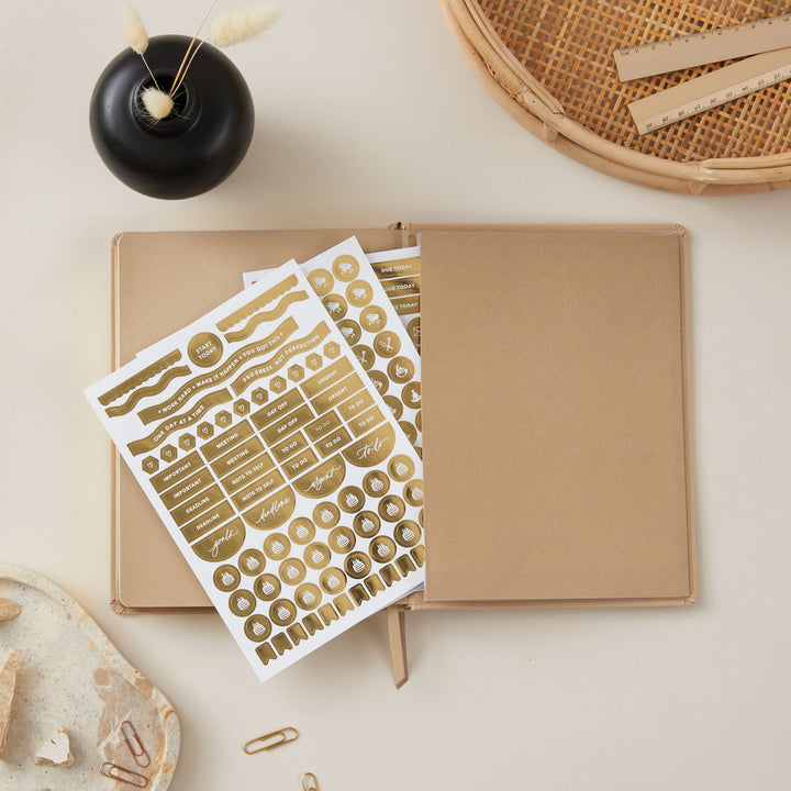 Elegant ivory fabric 2025 weekly planner with gold accents, featuring time-blocking for each day, to-do lists, note space, and pages for monthly goals and budgets.