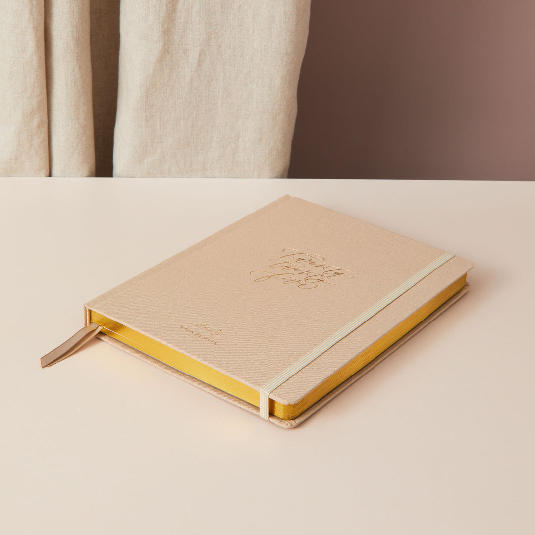 2025 weekly planner in ivory fabric with gold details, featuring equal time-blocking space for each day, to-do lists, and pages for monthly goals and budget planning.