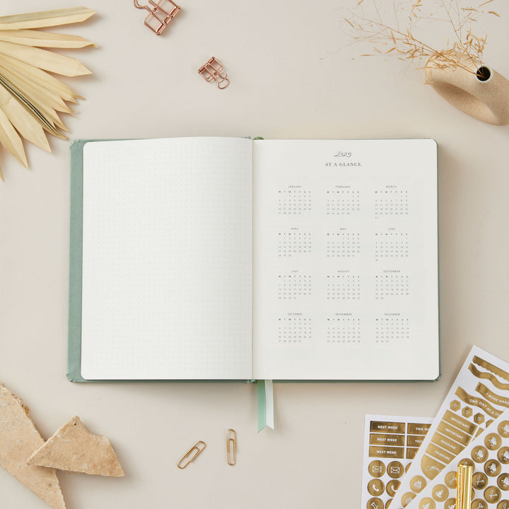 2025 planner with a sage green vegan leather cover and gold accents, featuring equal space for time-blocking each day, to-do lists, and monthly budget and goal pages.