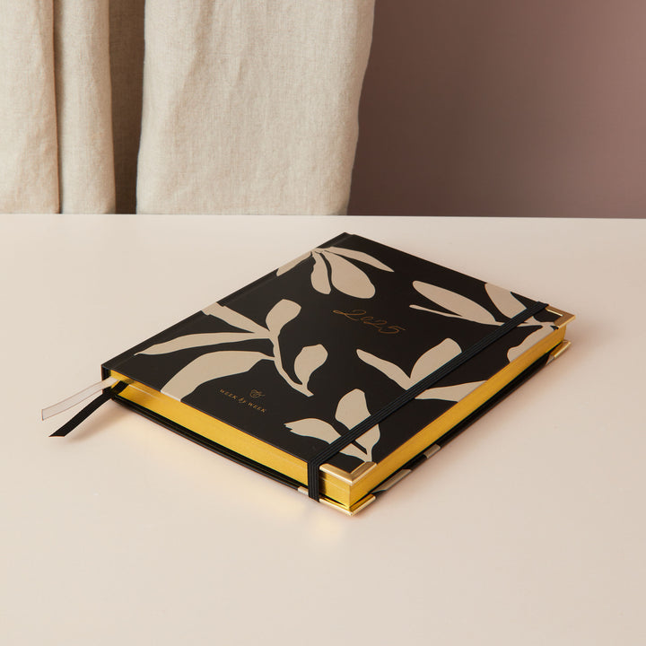 Minimalist floral 2025 weekly planner with a gold foil cover and gold edging, offering week-to-view pages, time blocking, to-do lists, and sections for notes.