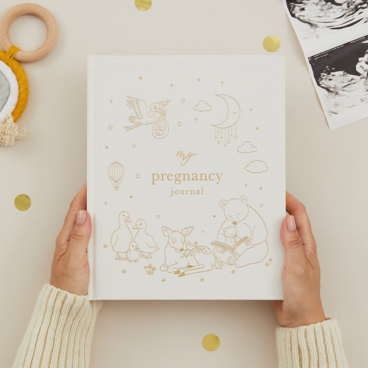 Pregnancy journal held by hands with baby items on a light background