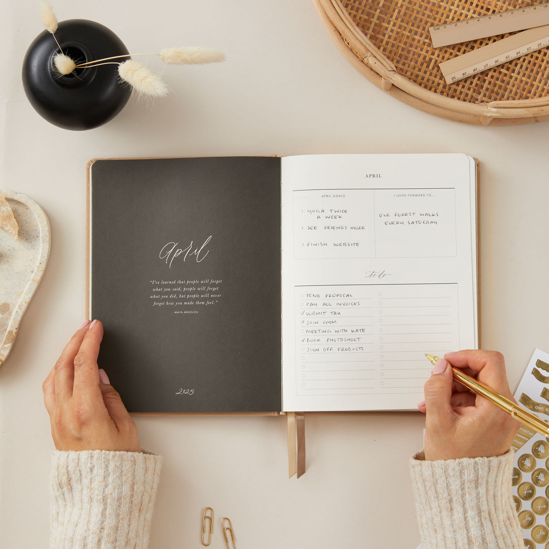Stylish 2025 weekly planner with an ivory fabric cover and gold details, offering daily time blocking, to-do lists, note space, and monthly goals and budgeting.
