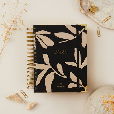 Floral 2025 daily planner with ring binding and gold accents, featuring a flower design on the cover, elegant gold details, and a durable spiral binding for easy page turning.