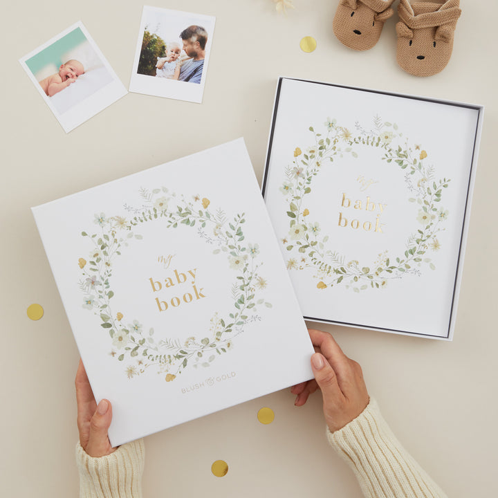 Two baby books with floral designs and text, held by a person on a light background.