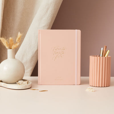 2025 weekly planner with a soft pink vegan leather cover and gold details, featuring time-blocking with equal space for each day, to-do lists, notes, and monthly goals and budget pages.