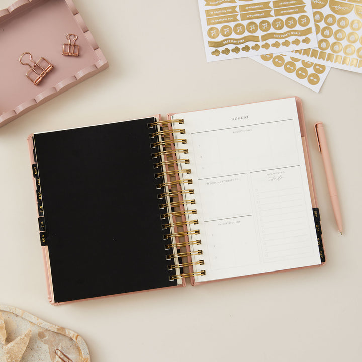 Pink day-to-page 2025 ring-bound planner open to a monthly overview page, providing a clear layout for scheduling and planning the month ahead.