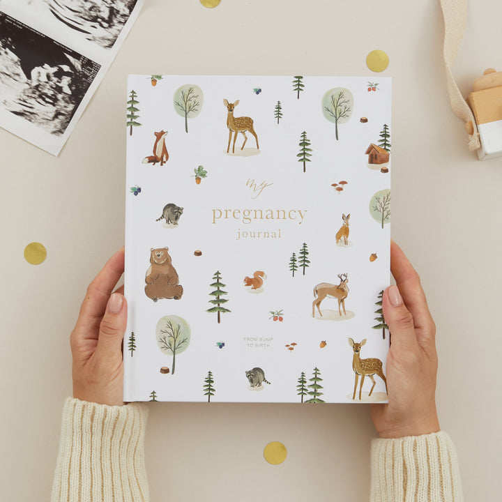 Pregnancy journal with nature-themed design held by hands on a light background