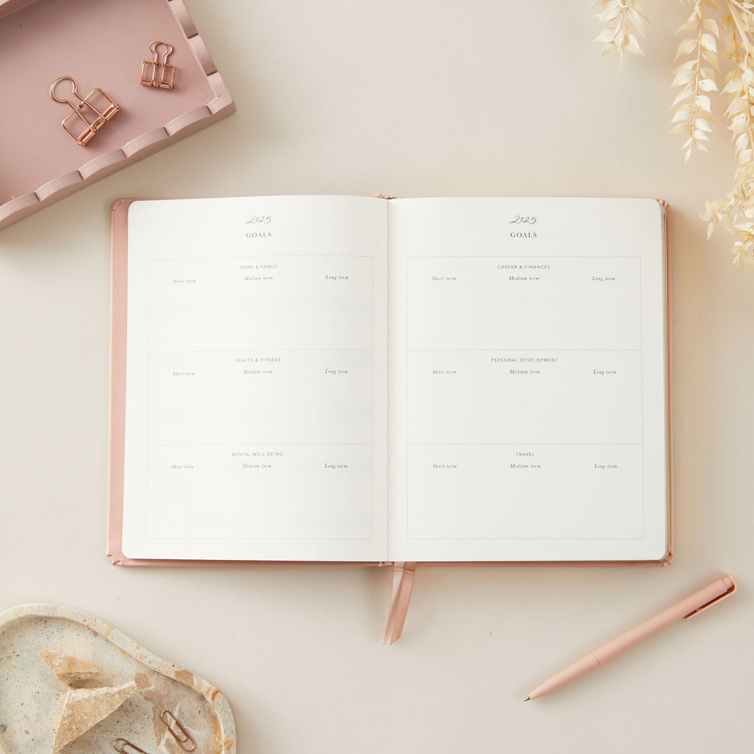 2025 planner with a soft pink vegan leather cover and gold accents, featuring equal space for time-blocking each day, to-do lists, notes, and monthly budget and goal pages.