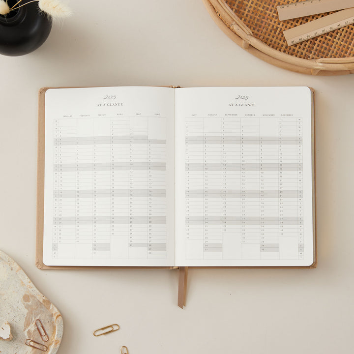 Ivory fabric 2025 planner with gold details, providing equal time-blocking space for each day of the week, to-do lists, and dedicated monthly goals and budget pages.