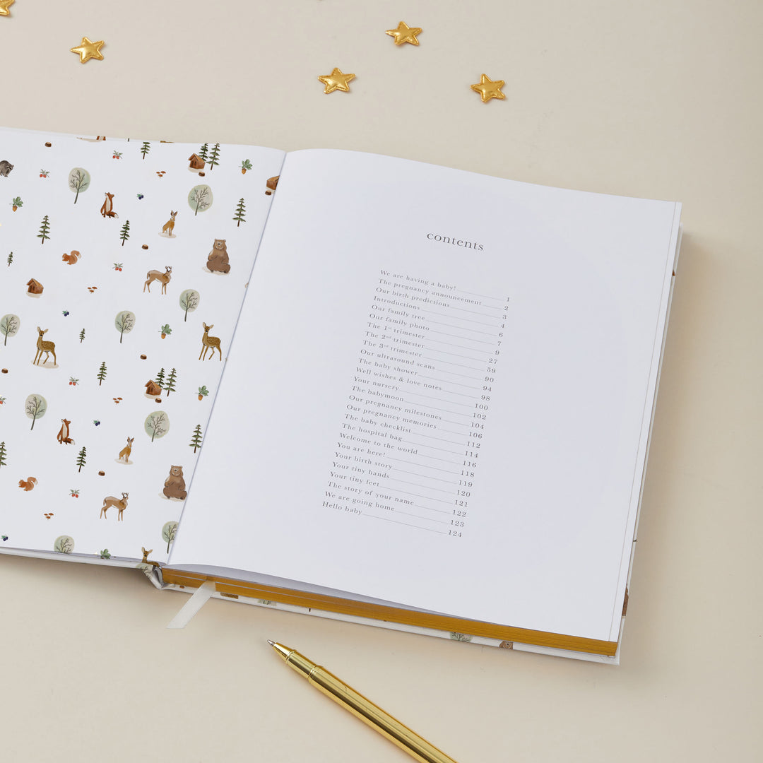 Open pregnancy journal with animal illustrations on one page and a table of contents on the other, on a beige surface.