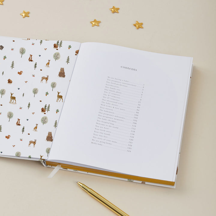 Open pregnancy journal with animal illustrations on one page and a table of contents on the other, on a beige surface.