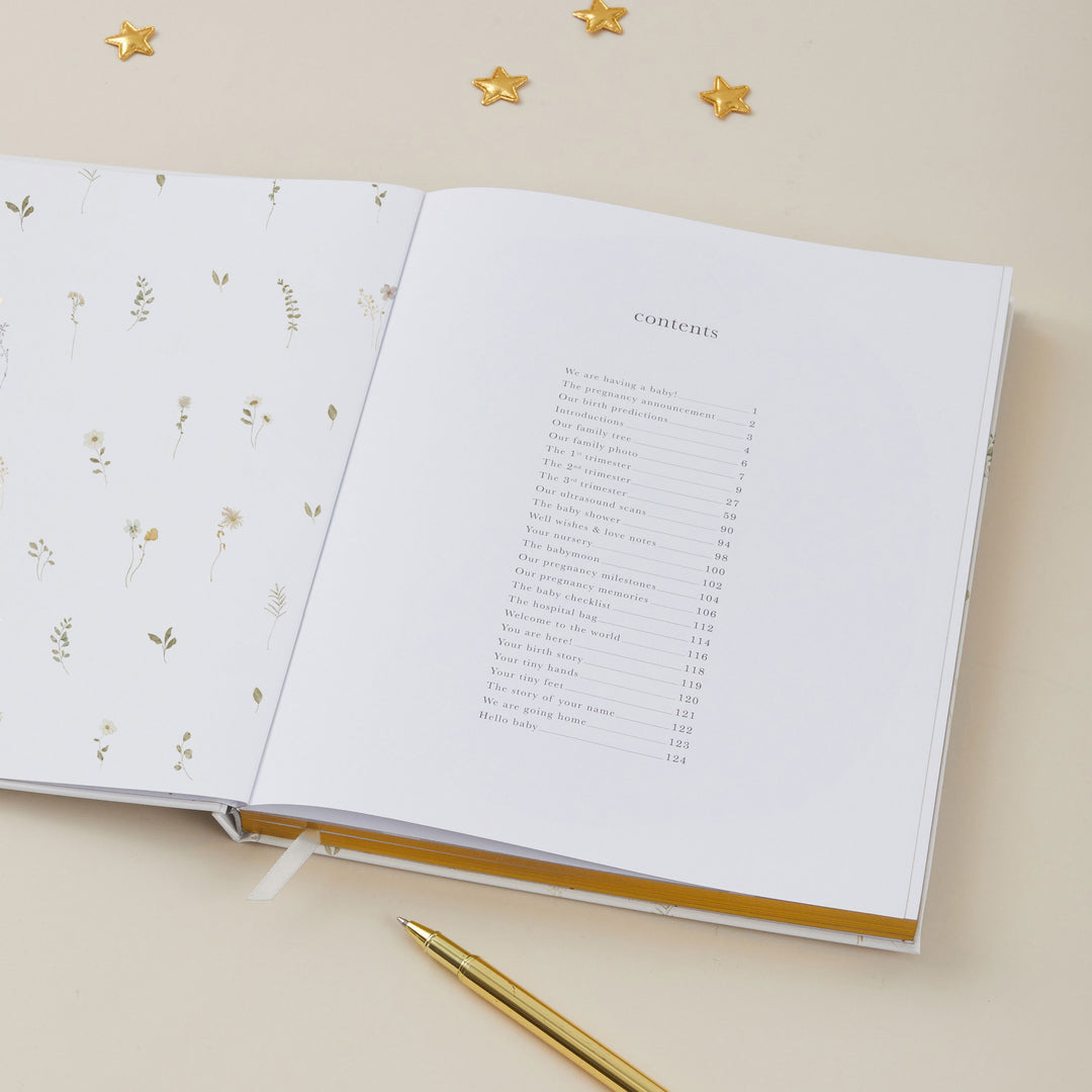 Open pregnancy journal with floral design on one page and text on the other, with a gold pen on a beige background.