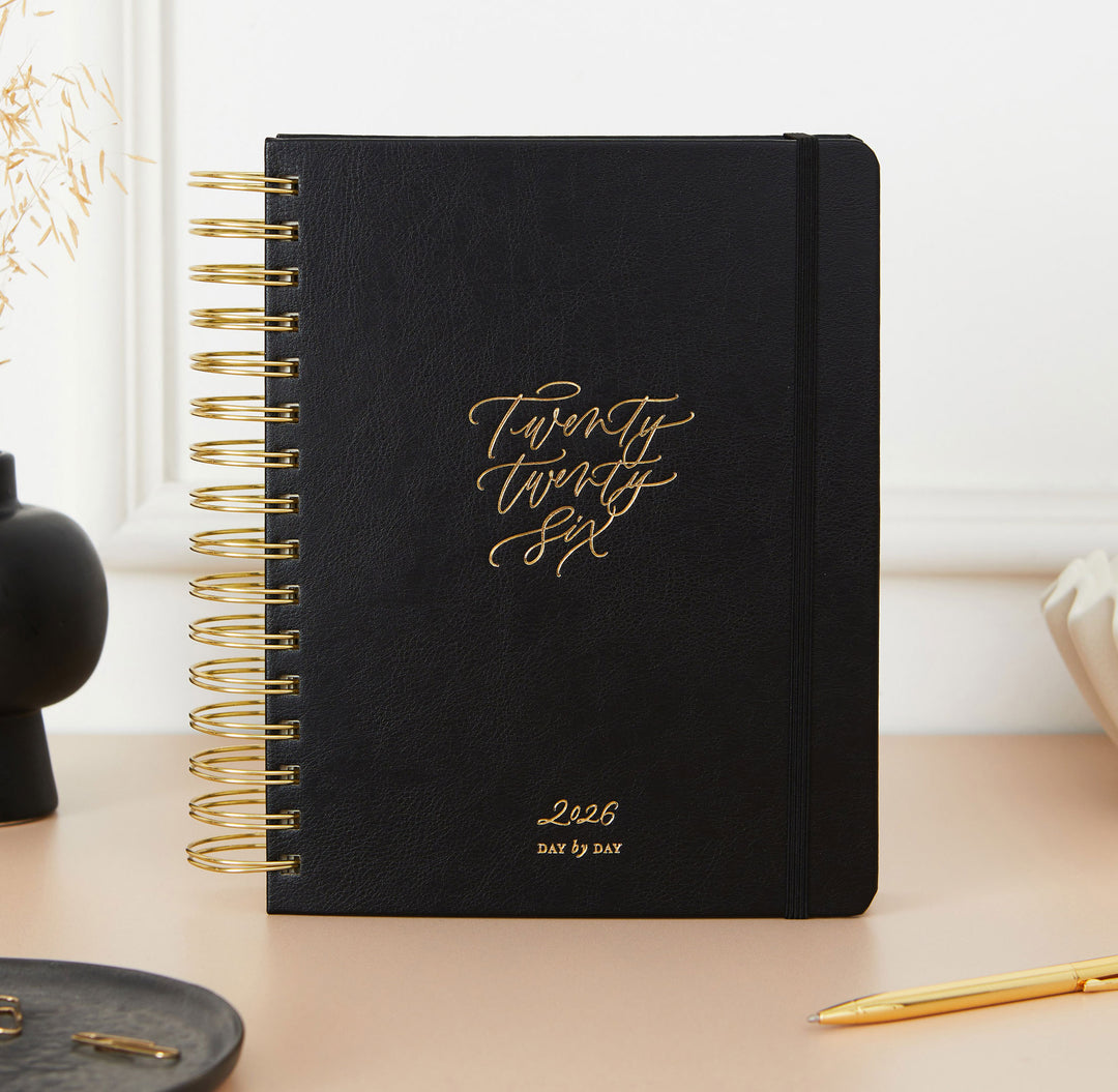 Black planner with gold text on a desk with decorative items