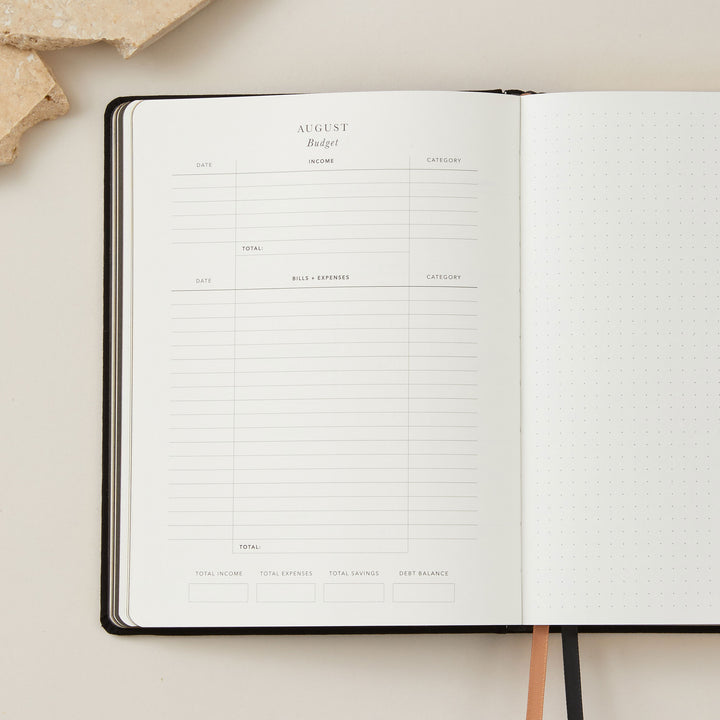Stylish 2025 weekly planner with a soft black vegan leather cover and gold accents, featuring time-blocking for each day of the week, to-do lists, and sections for notes and budgeting.