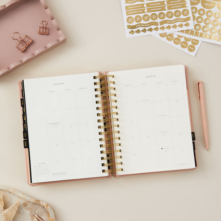 Pink day-to-page 2025 ring-bound planner open to a monthly overview page.