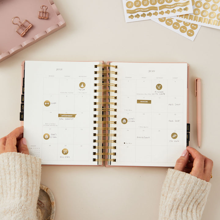 Daily 2025 ring-bound planner open to a monthly page, filled in with notes and with gold stickers for decorative and functional organisation.