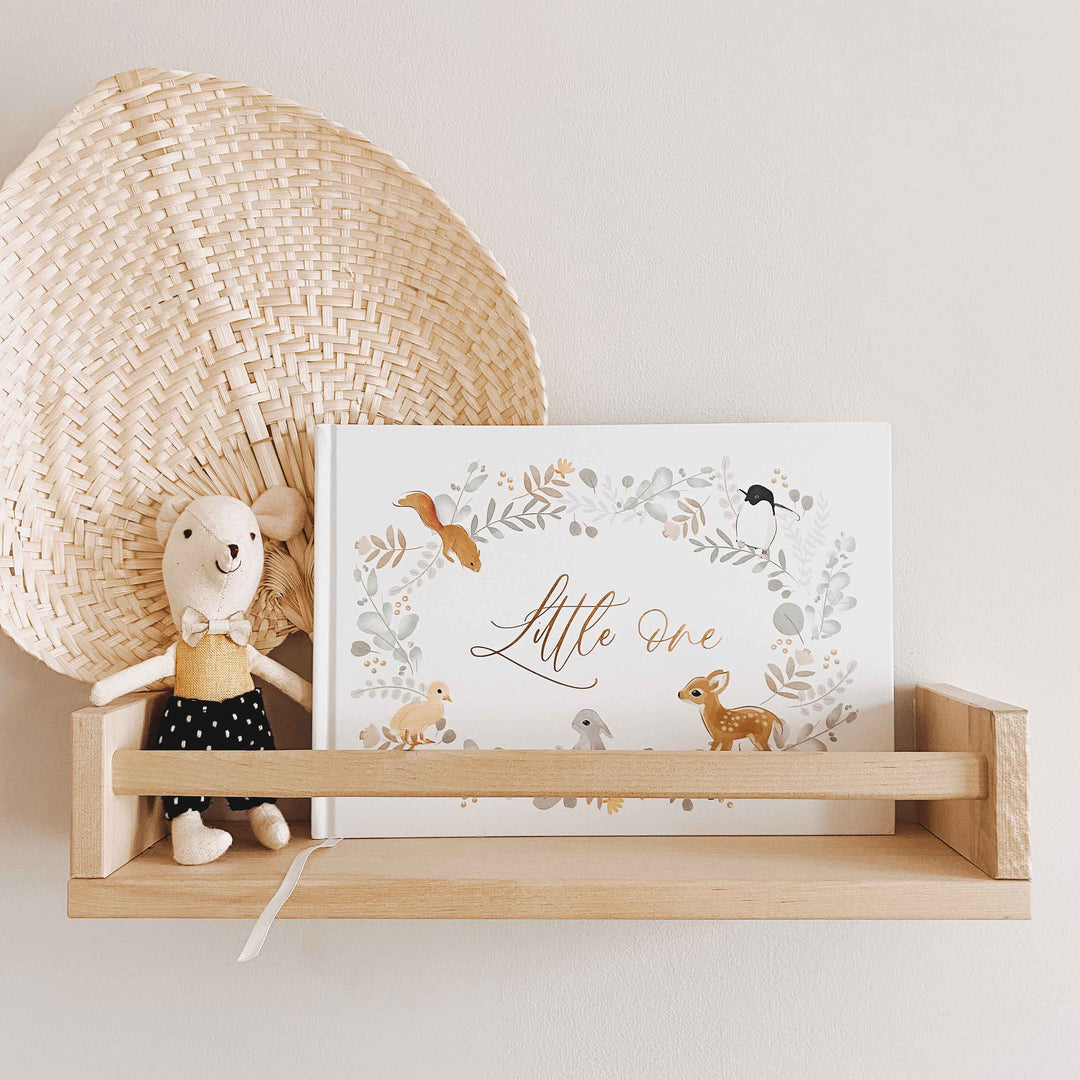 Baby memory book with cute animals on its cover and gold accents sitting on a baby nursery shelf, surrounded by soft toys.