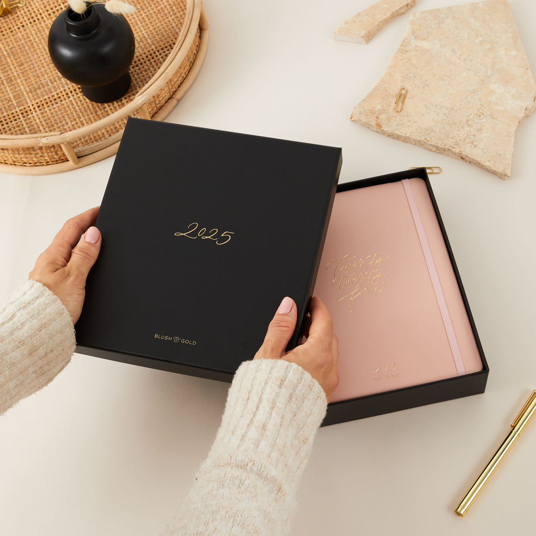 Pink vegan leather ring-bound daily planner with gold foiled details, packaged in a matching elegant gift box.