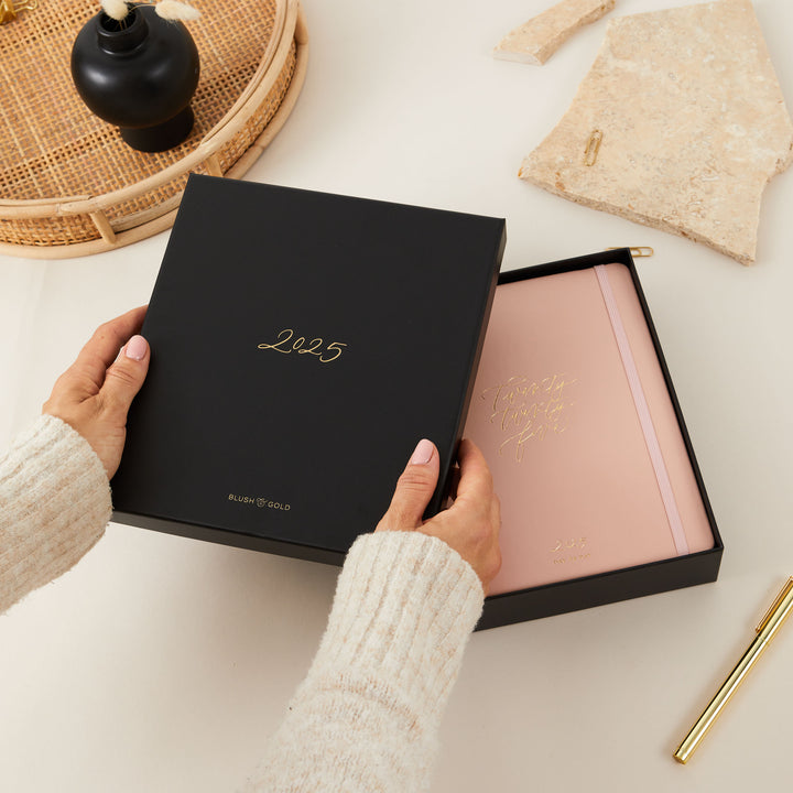 Pink vegan leather ring-bound daily planner with gold foiled details, packaged in a matching elegant gift box.