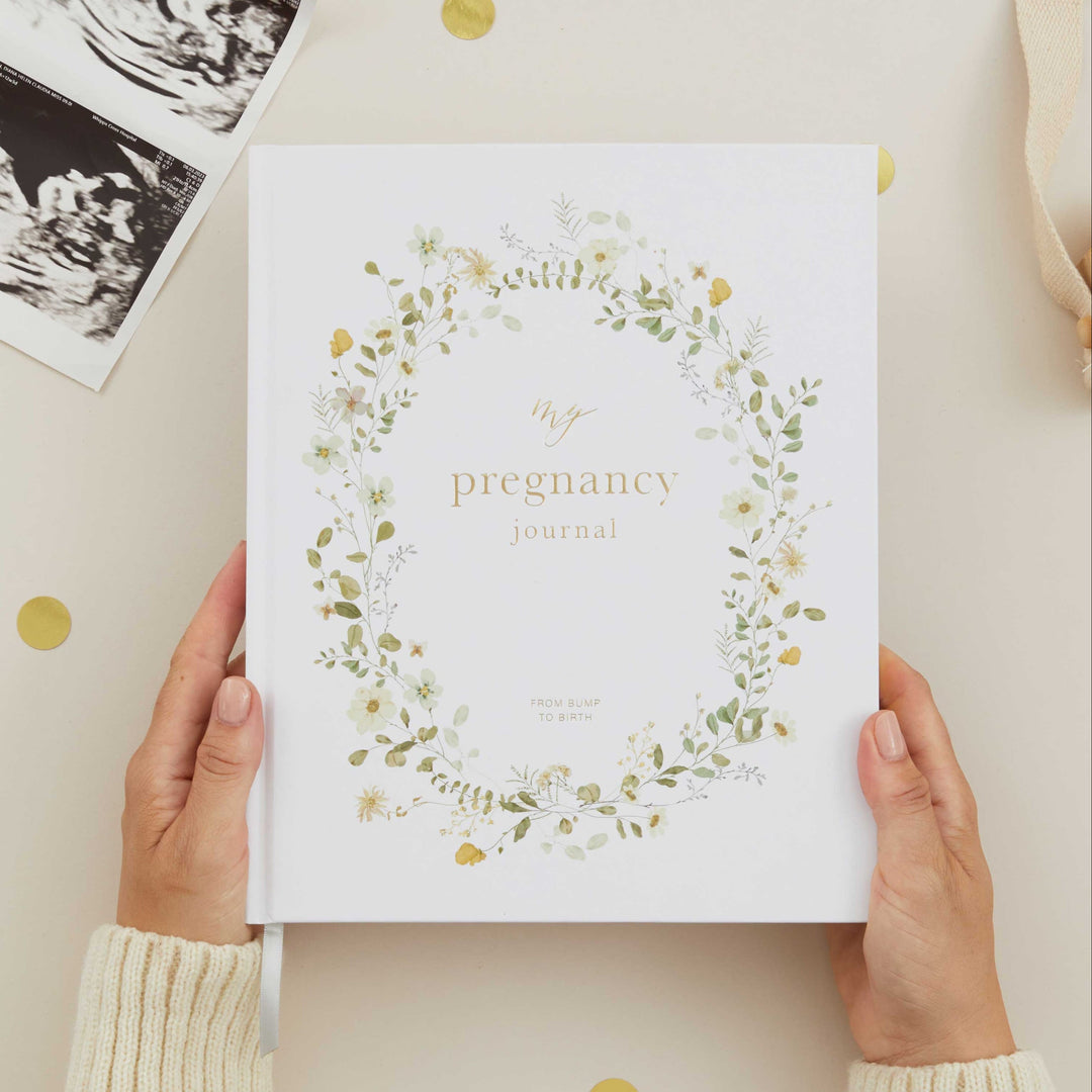Pregnancy journal with floral design held by hands on a light background