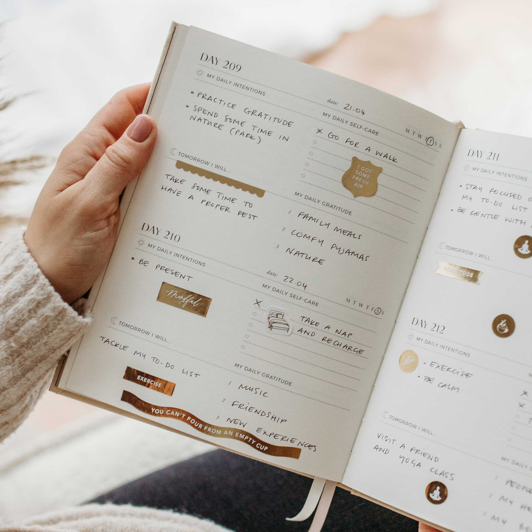 Daily pages filled in by hand with intentions and gratitude lists, decorated with gold stickers like "You can't pour from an empty cup"