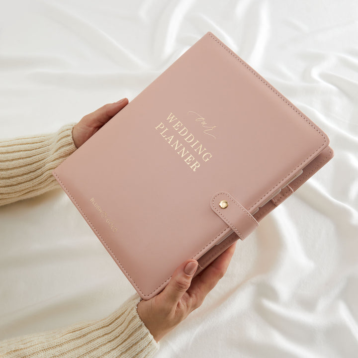 Woman holding a blush pink vegan leather wedding planner binder with gold foil cover text facing the camera