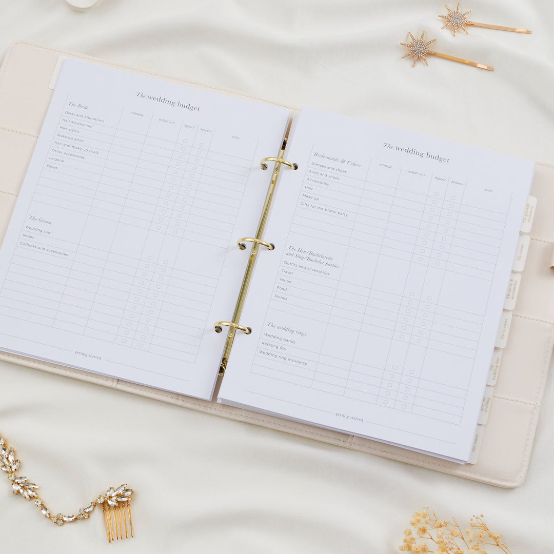 Open wedding planner binder showing a detailed wedding budget tracker double page spread covering bride, groom, bridesmaids and wedding rings