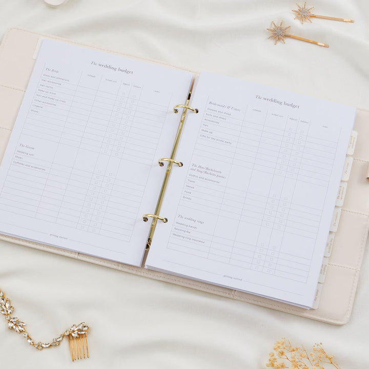 Open wedding planner binder showing a detailed wedding budget tracker double page spread covering bride, groom, bridesmaids and wedding rings